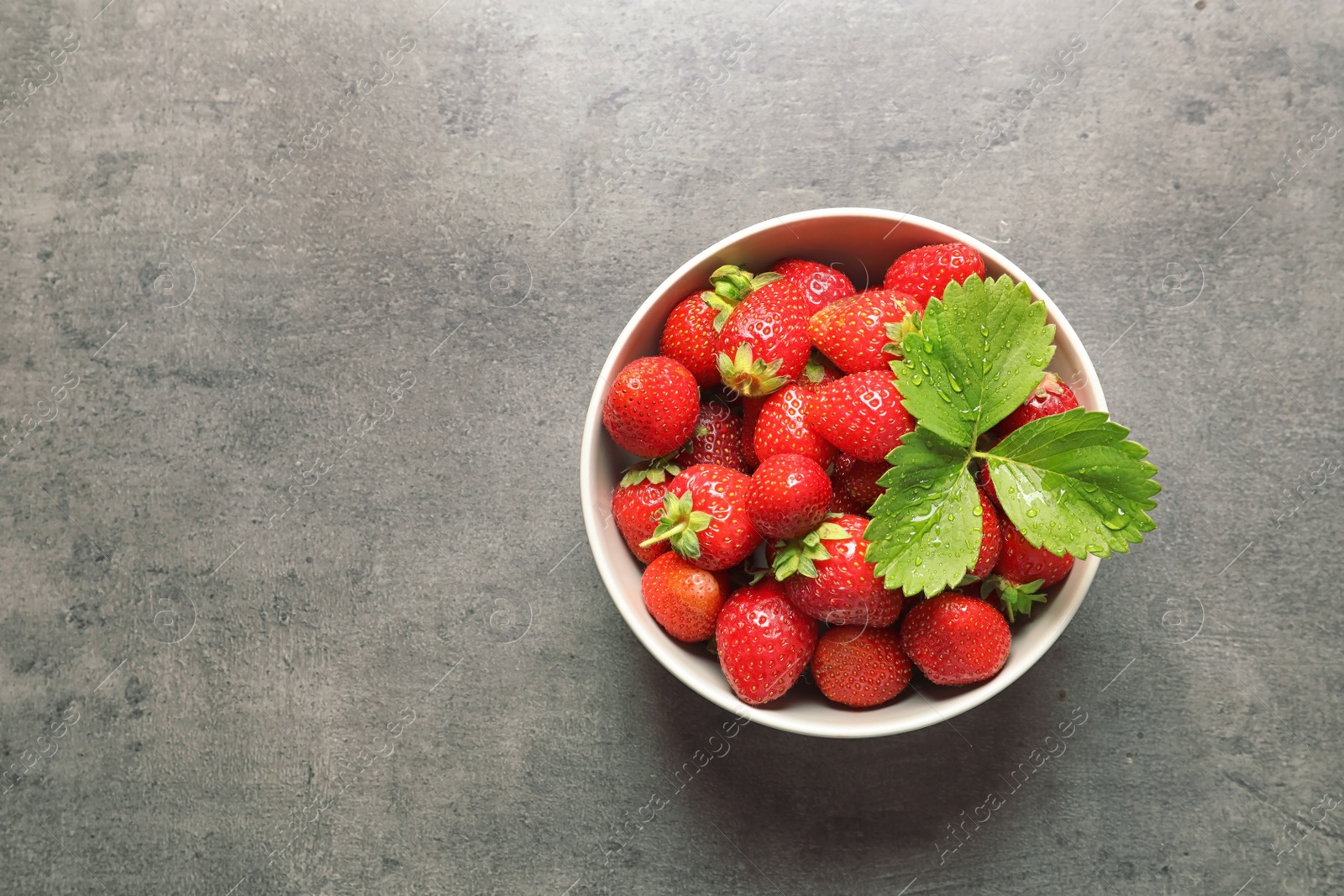 Photo of Bowl with ripe strawberries on grey background, top view