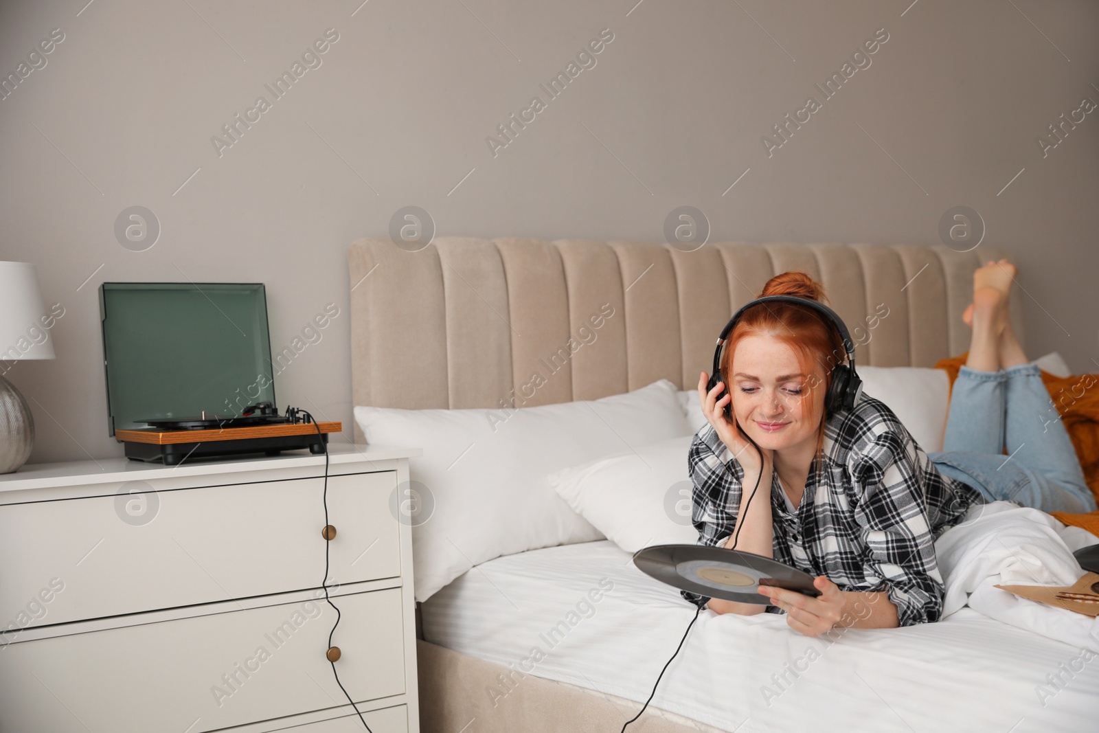 Photo of Young woman listening to music with turntable in bedroom