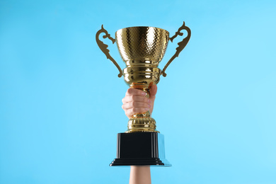 Woman holding gold trophy cup on light blue background, closeup