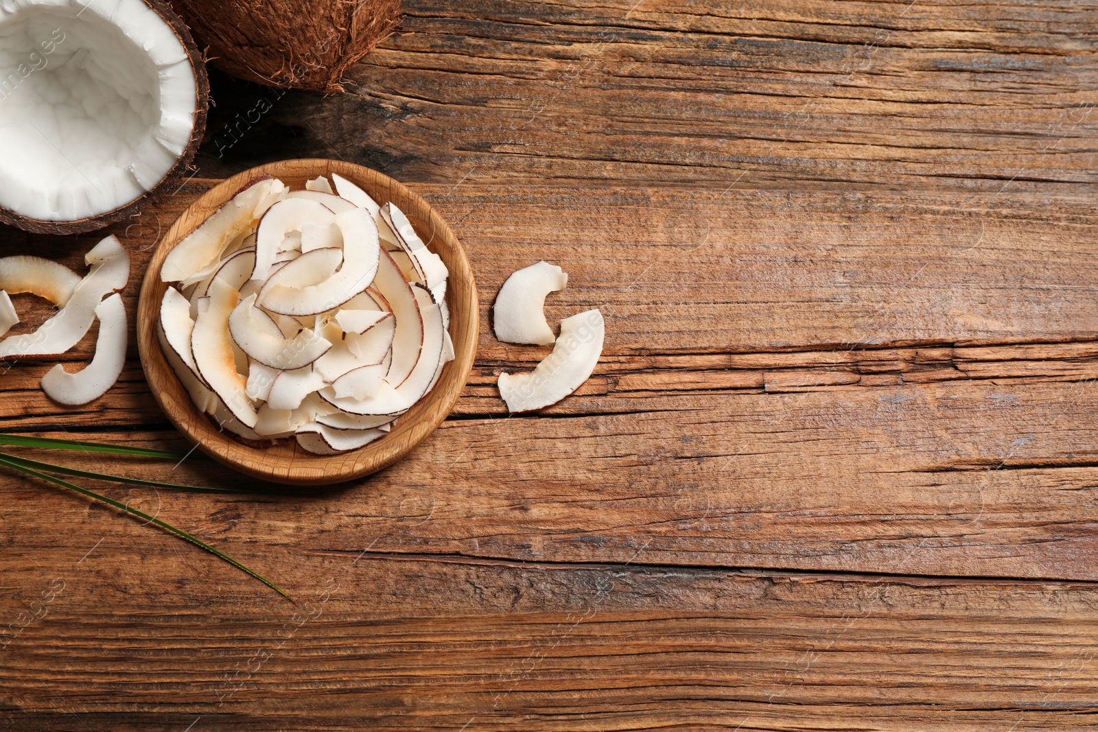 Photo of Tasty coconut chips on wooden table, flat lay. Space for text