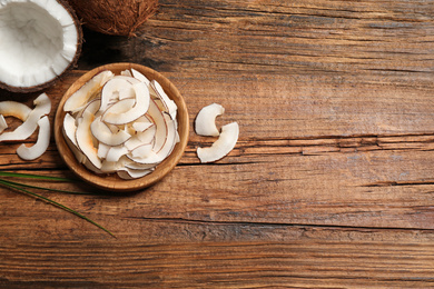 Tasty coconut chips on wooden table, flat lay. Space for text