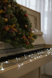 Photo of White piano with fairy lights and decorative wreath indoors, closeup. Christmas music