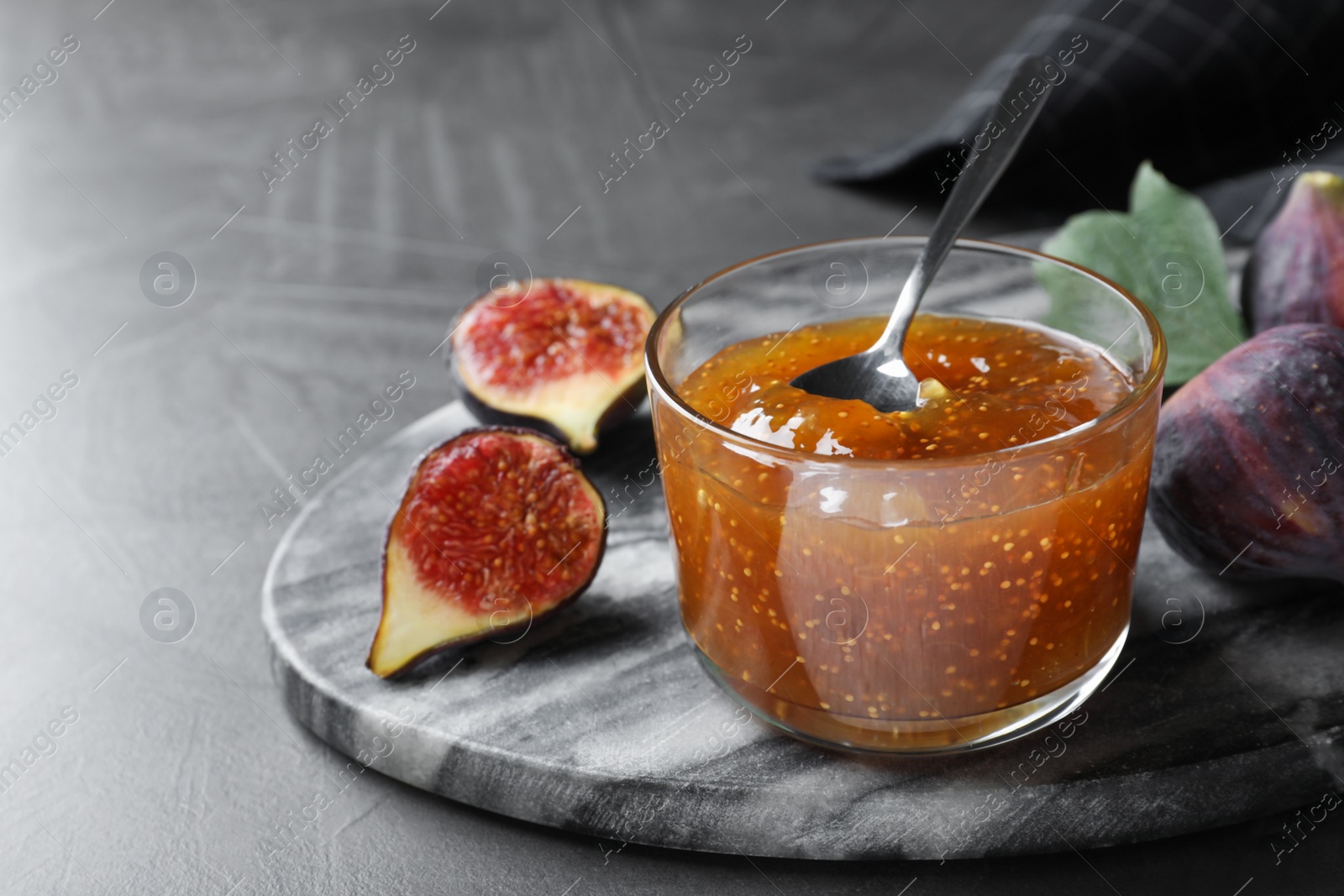 Photo of Delicious fig jam and fresh fruit on grey table, closeup. Space for text