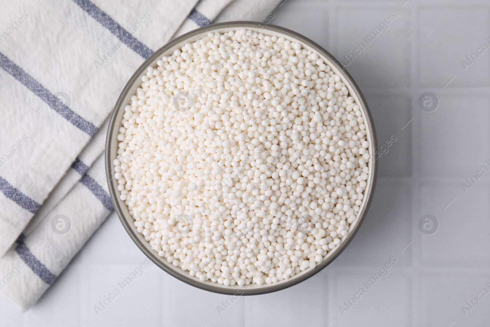 Photo of Tapioca pearls in bowl and towel on white tiled table, top view