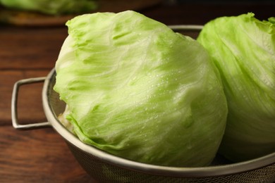 Photo of Colander with fresh green wet iceberg lettuce heads on wooden table, closeup