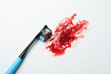 Photo of Toothbrush with paste and blood on white table, top view. Gum inflammation