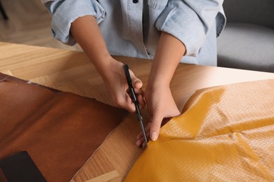 Photo of Woman cutting orange leather with scissors at wooden table, closeup