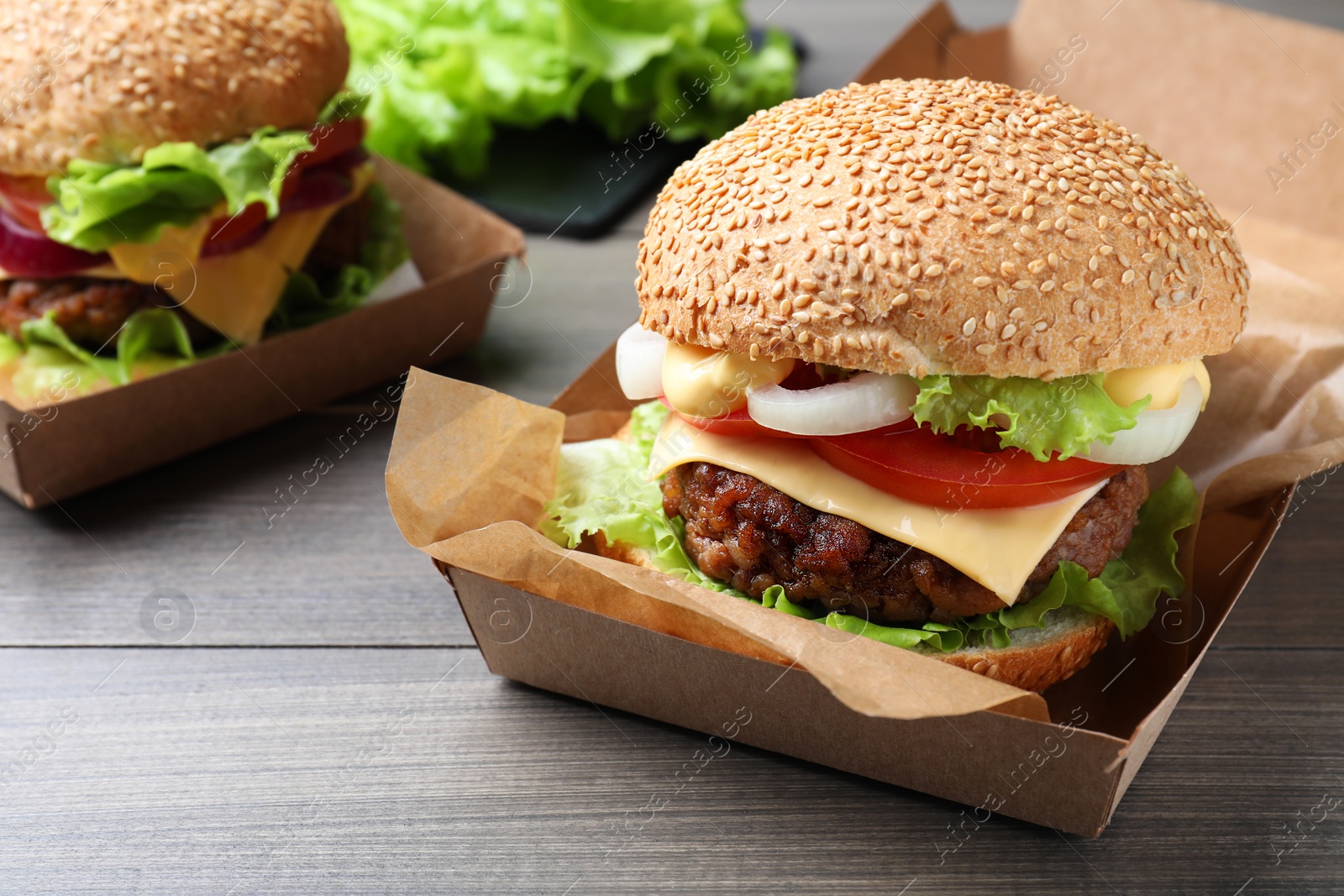 Photo of Delicious burgers in cardboard boxes on wooden table, closeup