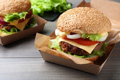 Photo of Delicious burgers in cardboard boxes on wooden table, closeup