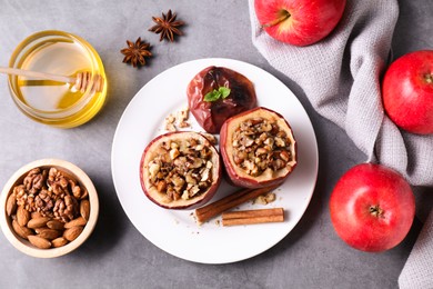 Tasty baked apples with nuts, honey and spices on gray table, flat lay