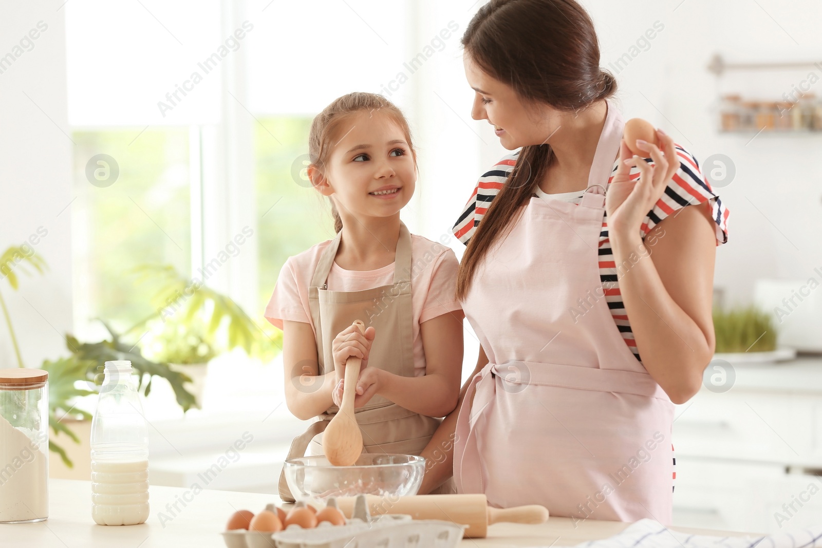 Photo of Mother and her daughter making dough at table in kitchen