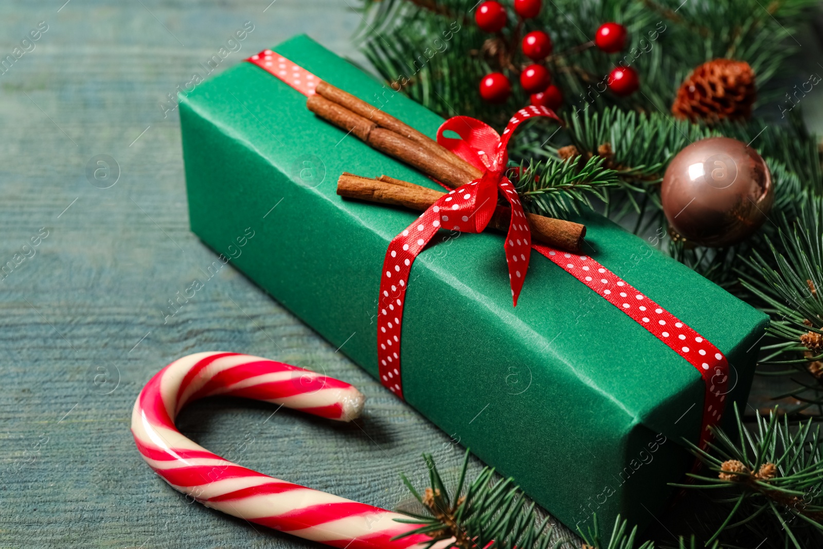 Photo of Christmas gift box, candy cane and festive decor on blue wooden table, closeup