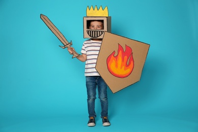 Photo of Cute little child in cardboard armor on color background