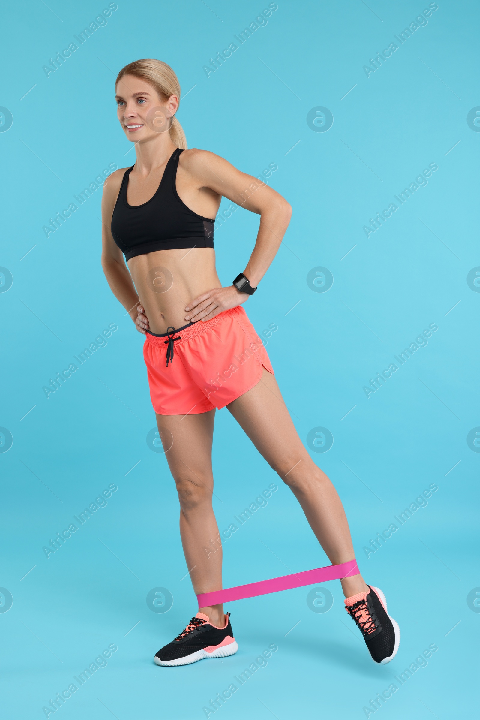 Photo of Woman exercising with elastic resistance band on light blue background