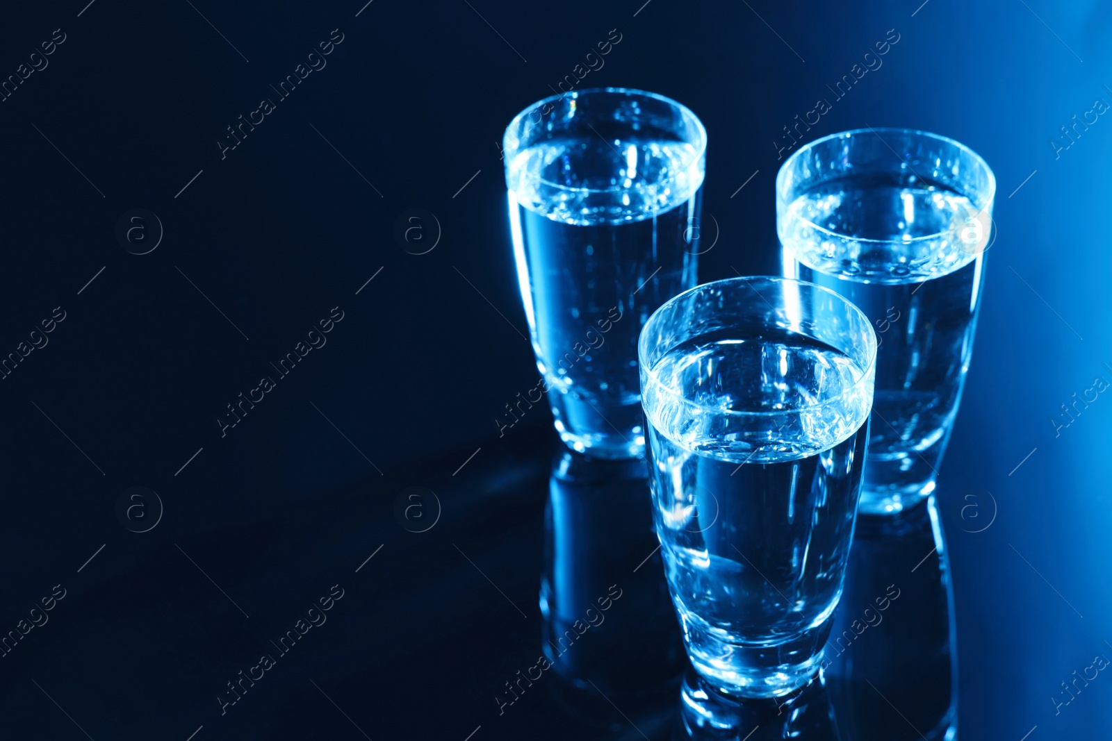 Photo of Glasses of vodka on dark table, space for text