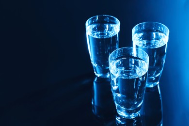 Photo of Glasses of vodka on dark table, space for text