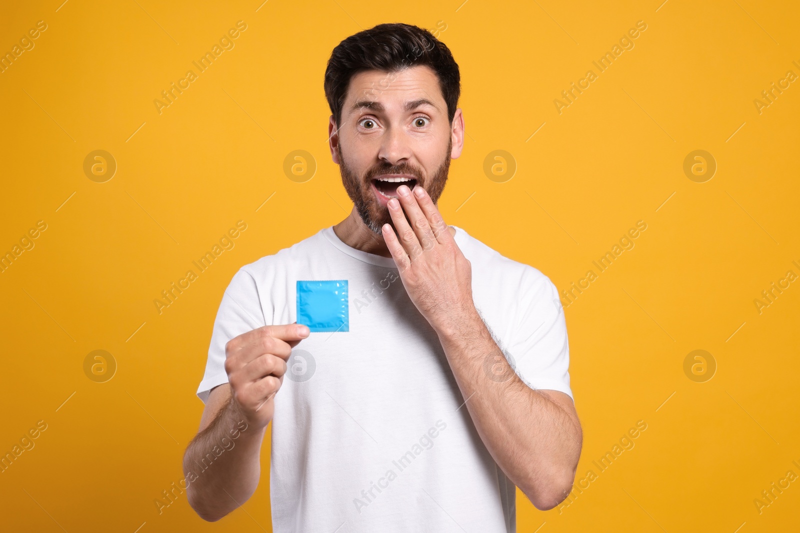 Photo of Emotional man holding condom on yellow background. Safe sex