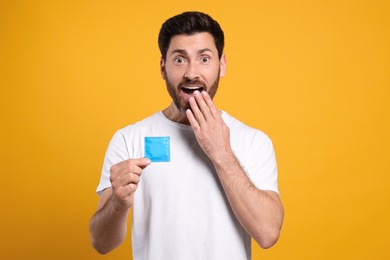 Photo of Emotional man holding condom on yellow background. Safe sex