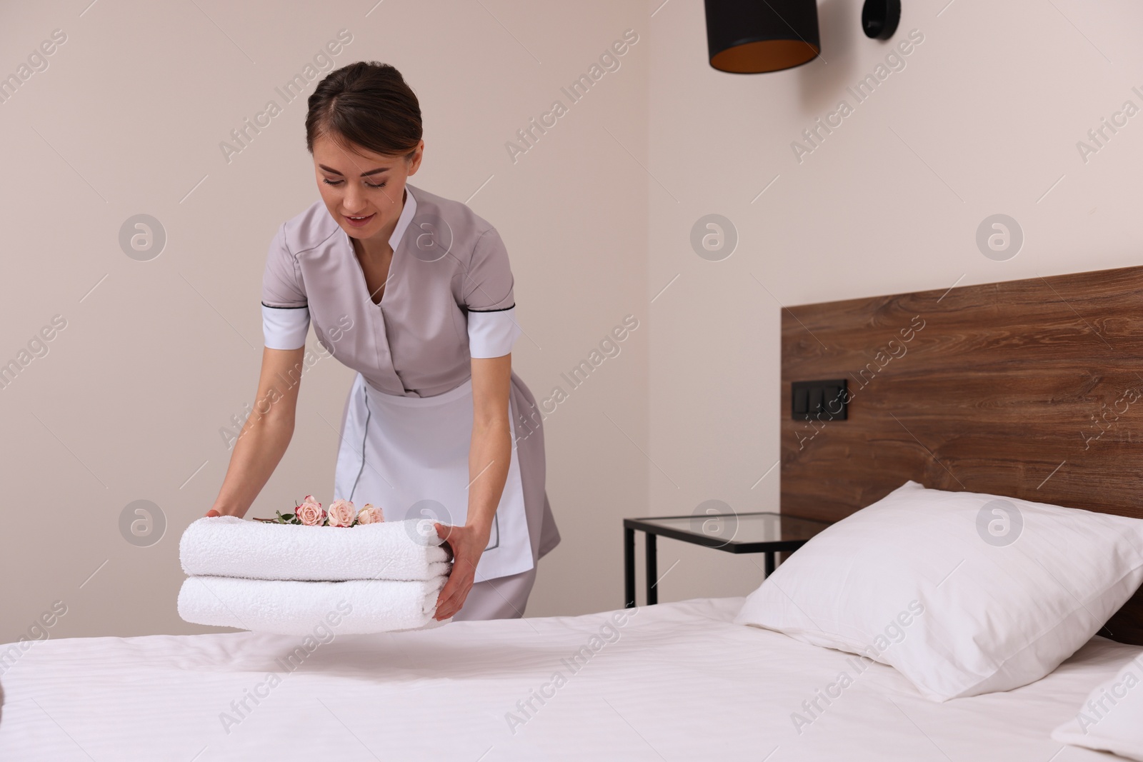 Photo of Beautiful chambermaid putting fresh towels on bed in hotel room