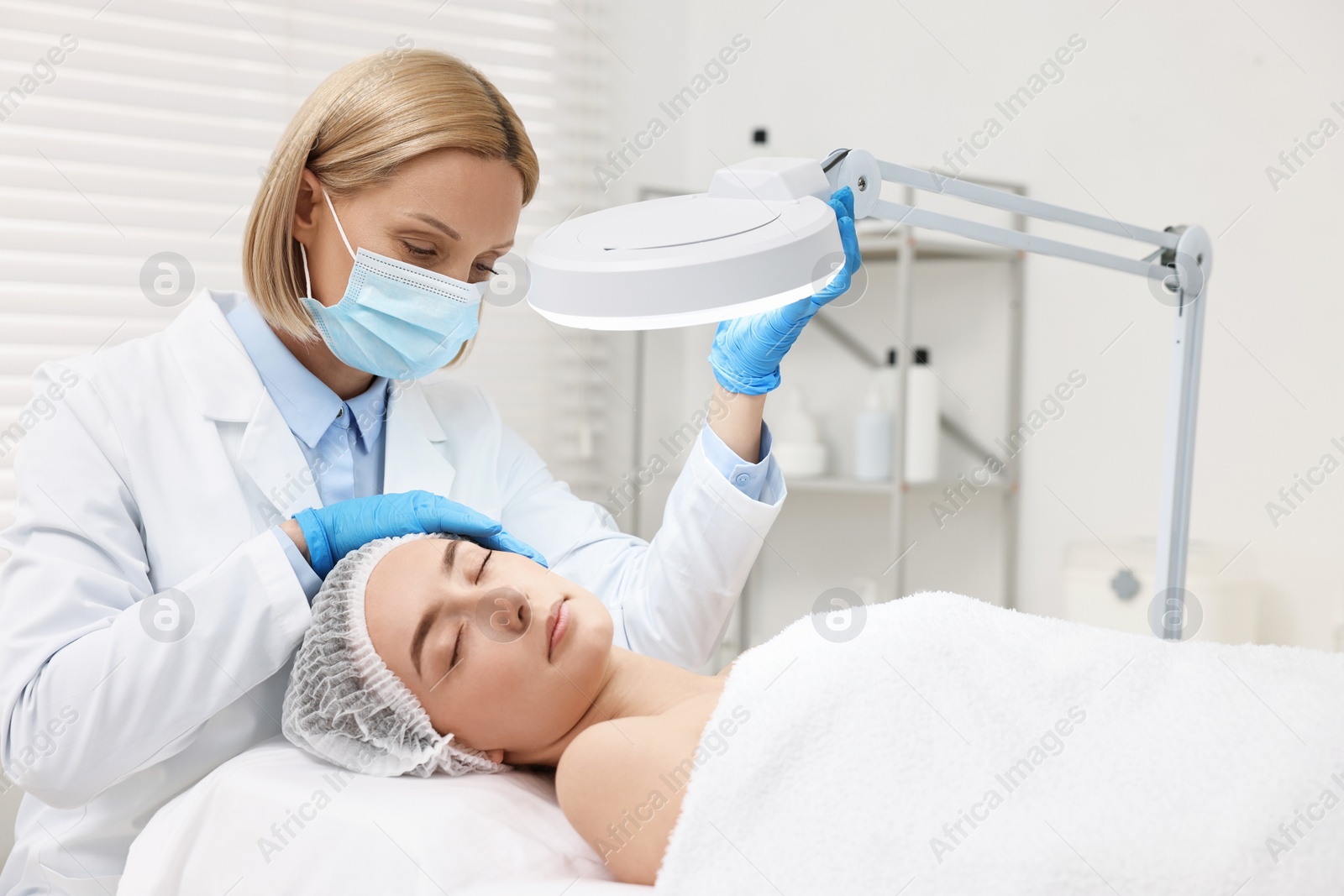 Photo of Dermatologist examining patient`s face under lamp in clinic