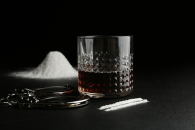 Photo of Glass of alcohol, cocaine and handcuffs on dark table