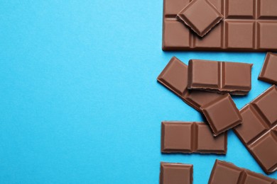 Photo of Pieces of delicious chocolate bars on light blue background, flat lay. Space for text