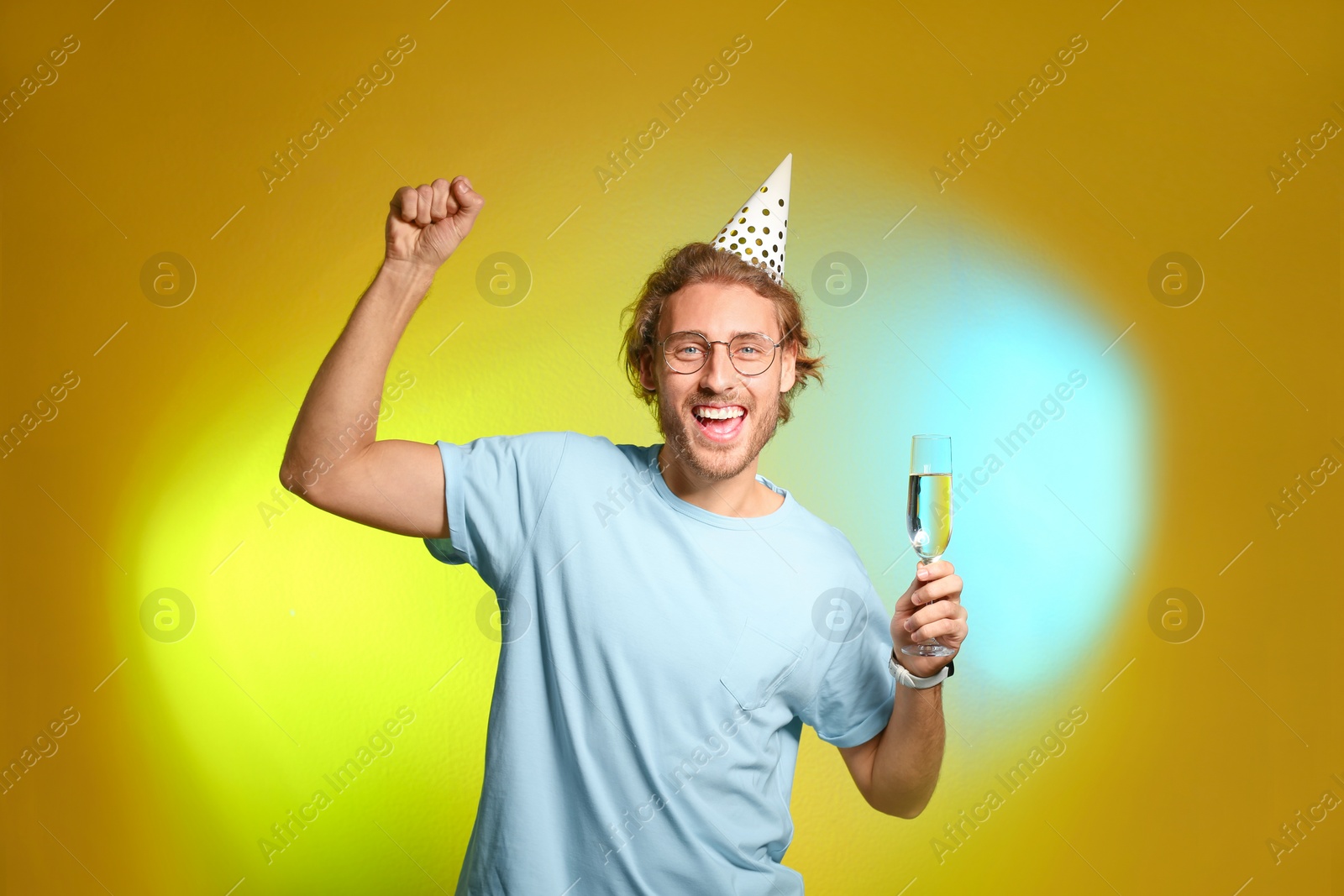 Photo of Portrait of happy man with party cap and champagne in glass on color background