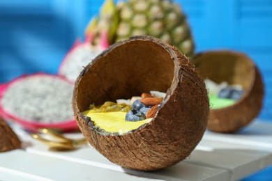 Photo of Tasty smoothie bowl with fresh blueberries and almonds served in coconut shell on white wooden table, closeup