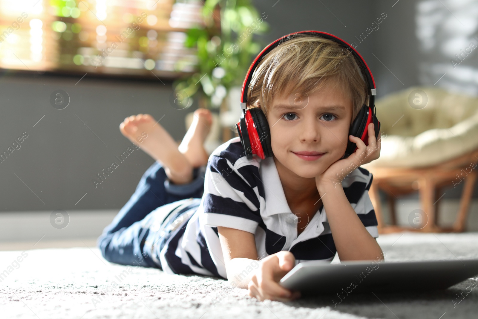 Photo of Cute little boy with headphones and tablet listening to audiobook at home