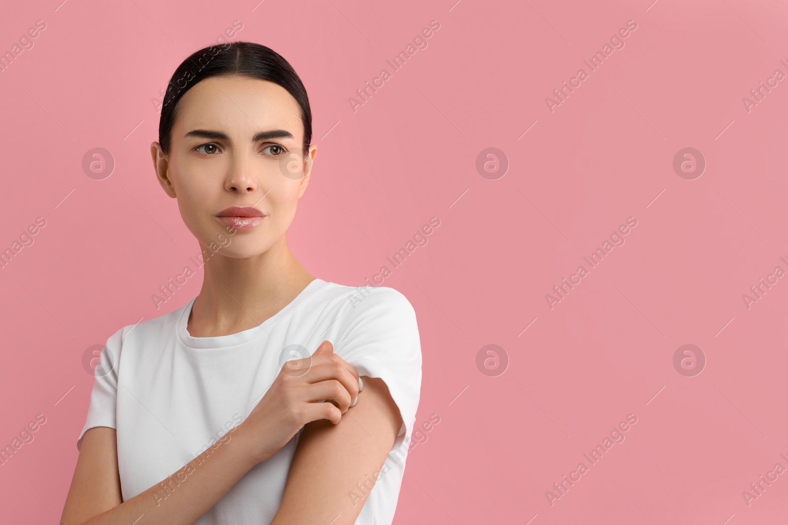 Photo of Woman with dry skin checking her arm on pink background, space for text