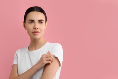 Woman with dry skin checking her arm on pink background, space for text