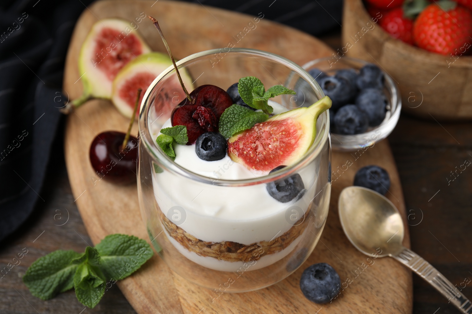 Photo of Glass with yogurt, berries, mint and granola on wooden table, closeup