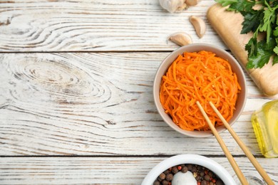 Photo of Delicious Korean carrot salad, oil, spices and parsley on white wooden table, flat lay. Space for text