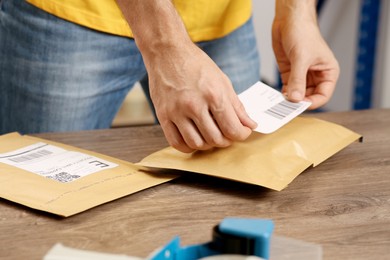 Photo of Post office worker sticking barcode on parcel at counter indoors, closeup