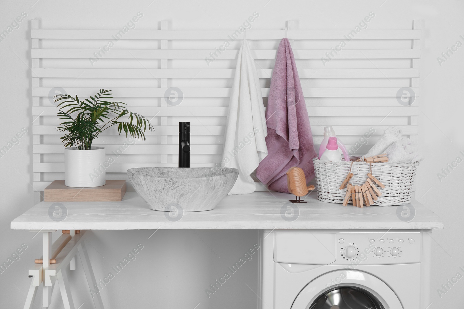 Photo of Laundry room interior with modern washing machine and stylish vessel sink on white wooden countertop