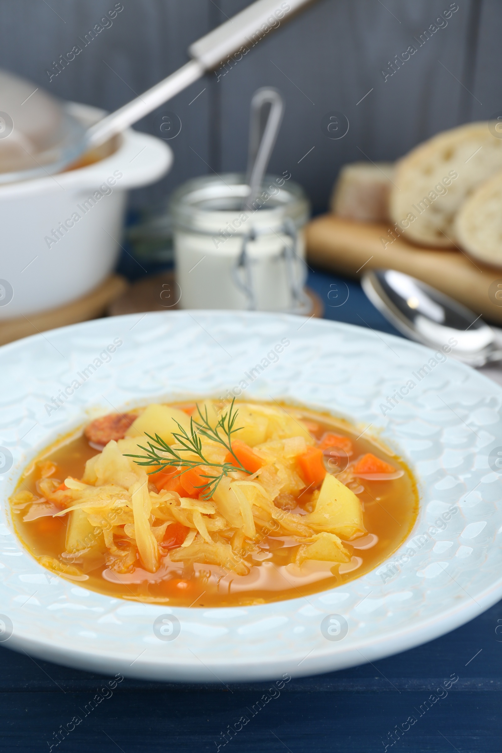 Photo of Delicious sauerkraut soup with carrot and dill on blue table, closeup