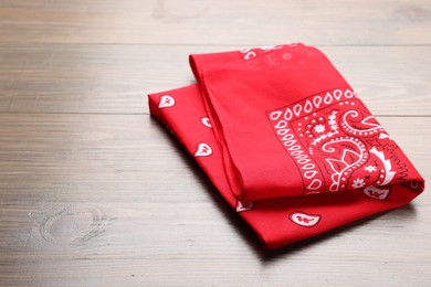 Photo of Folded red bandana with paisley pattern on wooden table, space for text