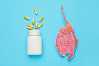 Paper cutout of small intestine and bottle with pills on turquoise background, flat lay