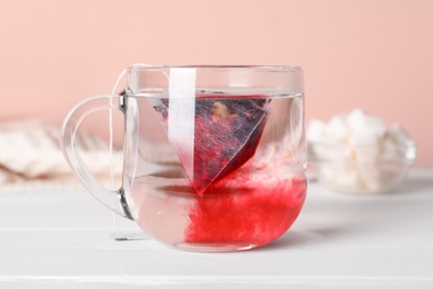 Tea bag in glass cup with water on white wooden table