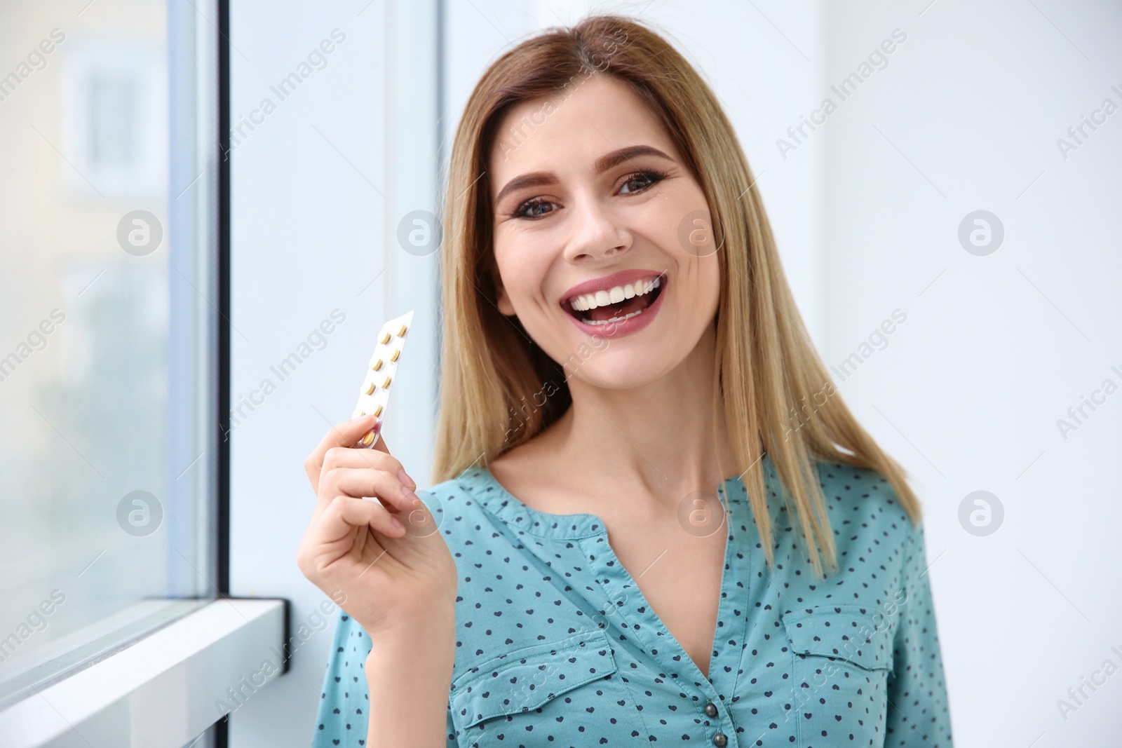 Photo of Young woman holding blister with vitamins indoors