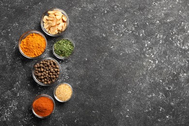Photo of Glass bowls with different spices on grey textured table, flat lay. Space for text