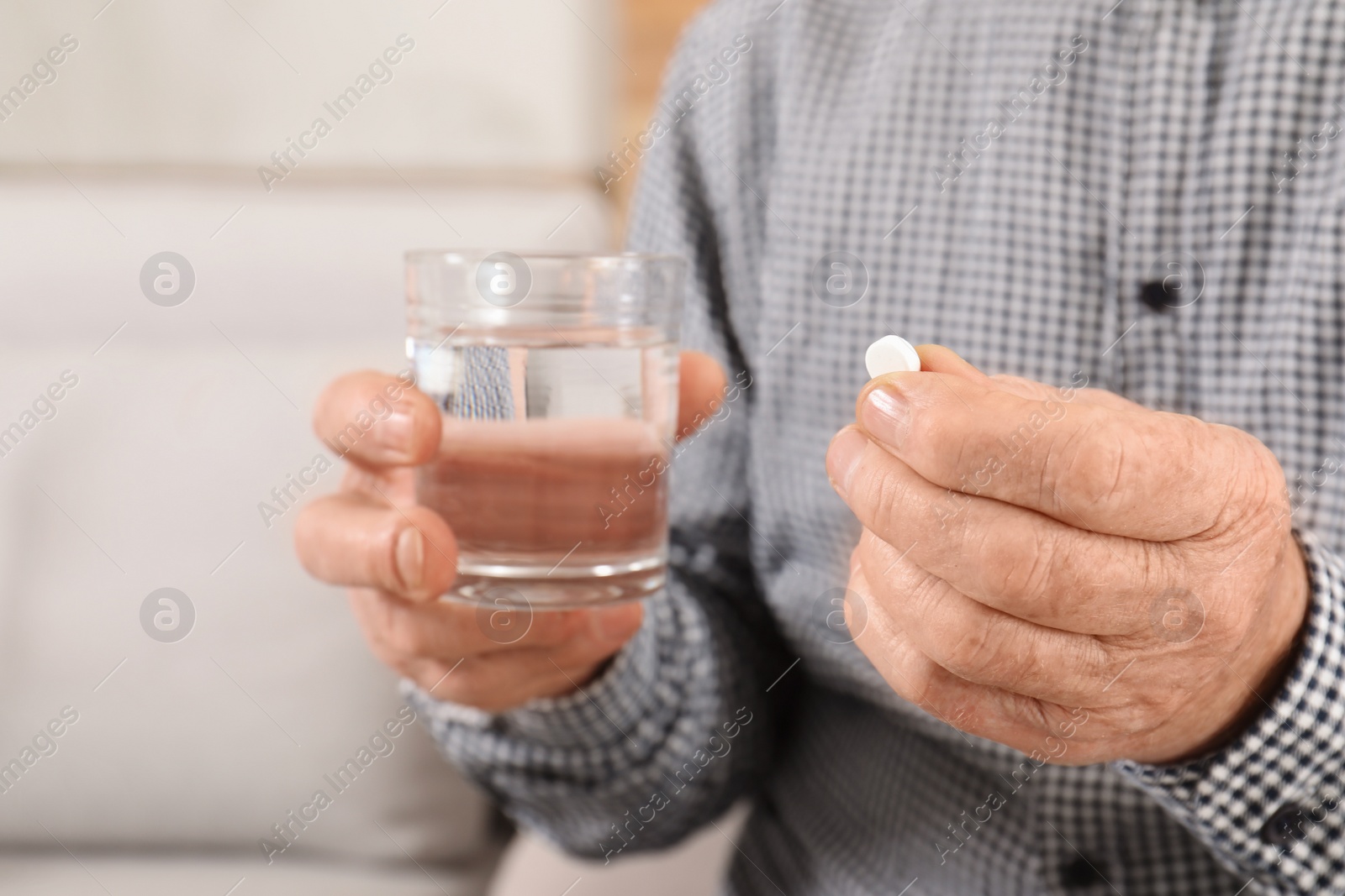 Photo of Senior man holding pill and glass of water indoors, closeup