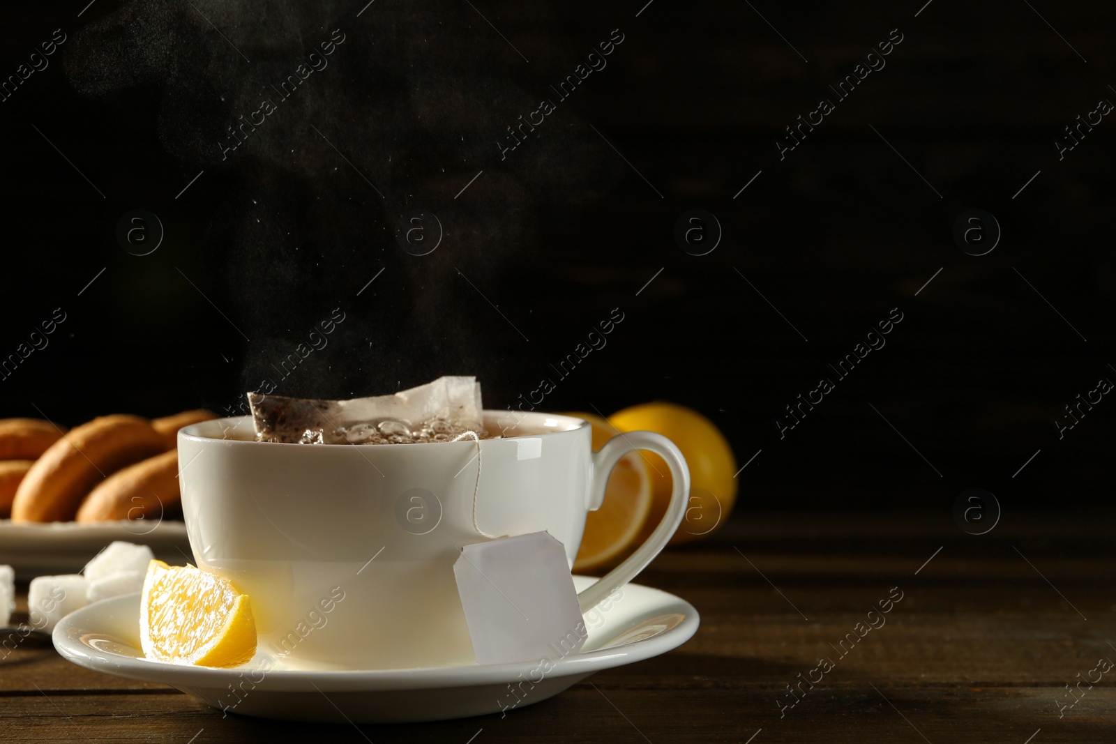 Photo of Tea bag in ceramic cup of hot water and lemon on dark wooden table. Space for text