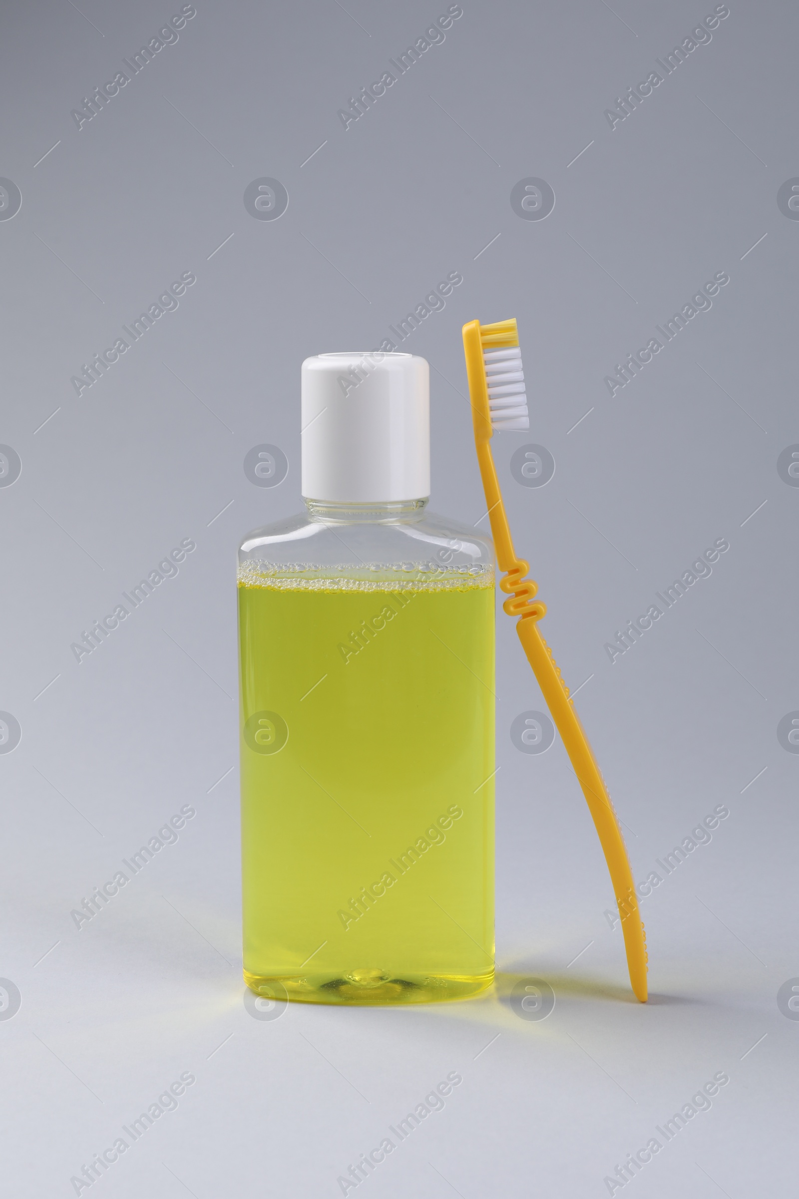 Photo of Fresh mouthwash in bottle and toothbrush on grey background