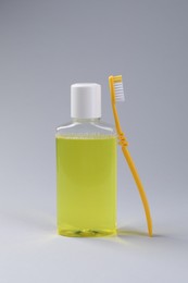 Photo of Fresh mouthwash in bottle and toothbrush on grey background