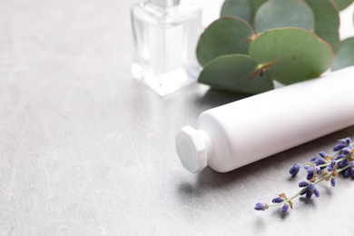 Photo of Tube of hand cream, eucalyptus branch and lavender on light grey table, space for text