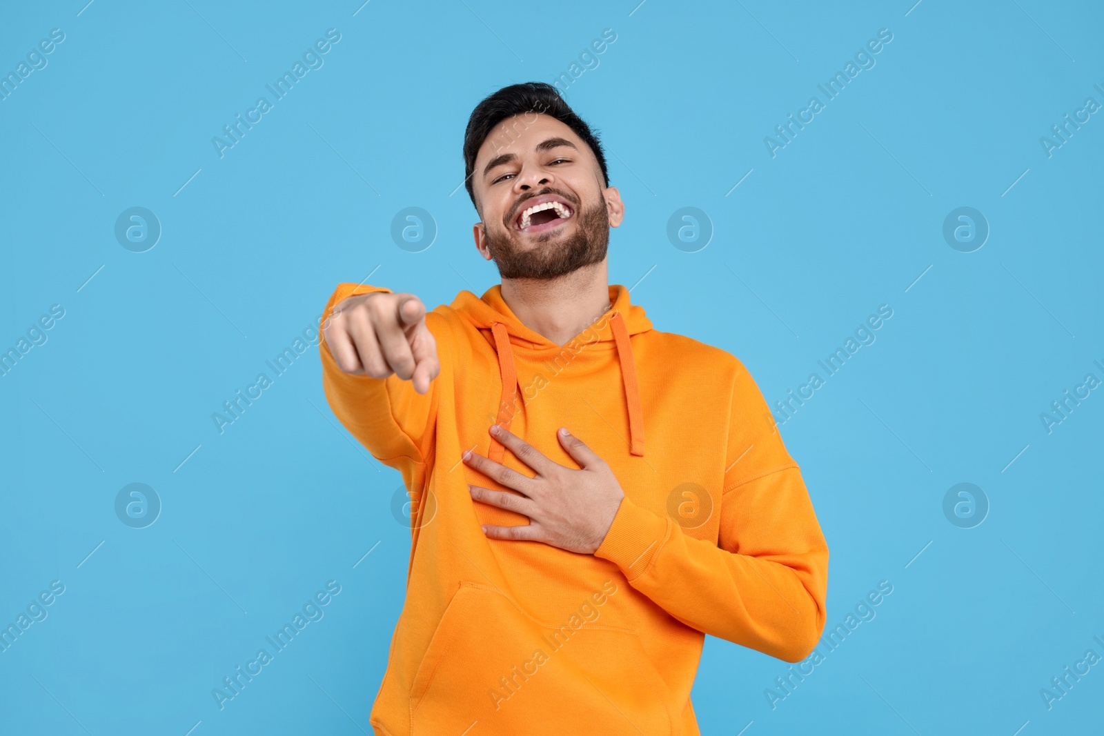 Photo of Handsome young man laughing while pointing at something on light blue background