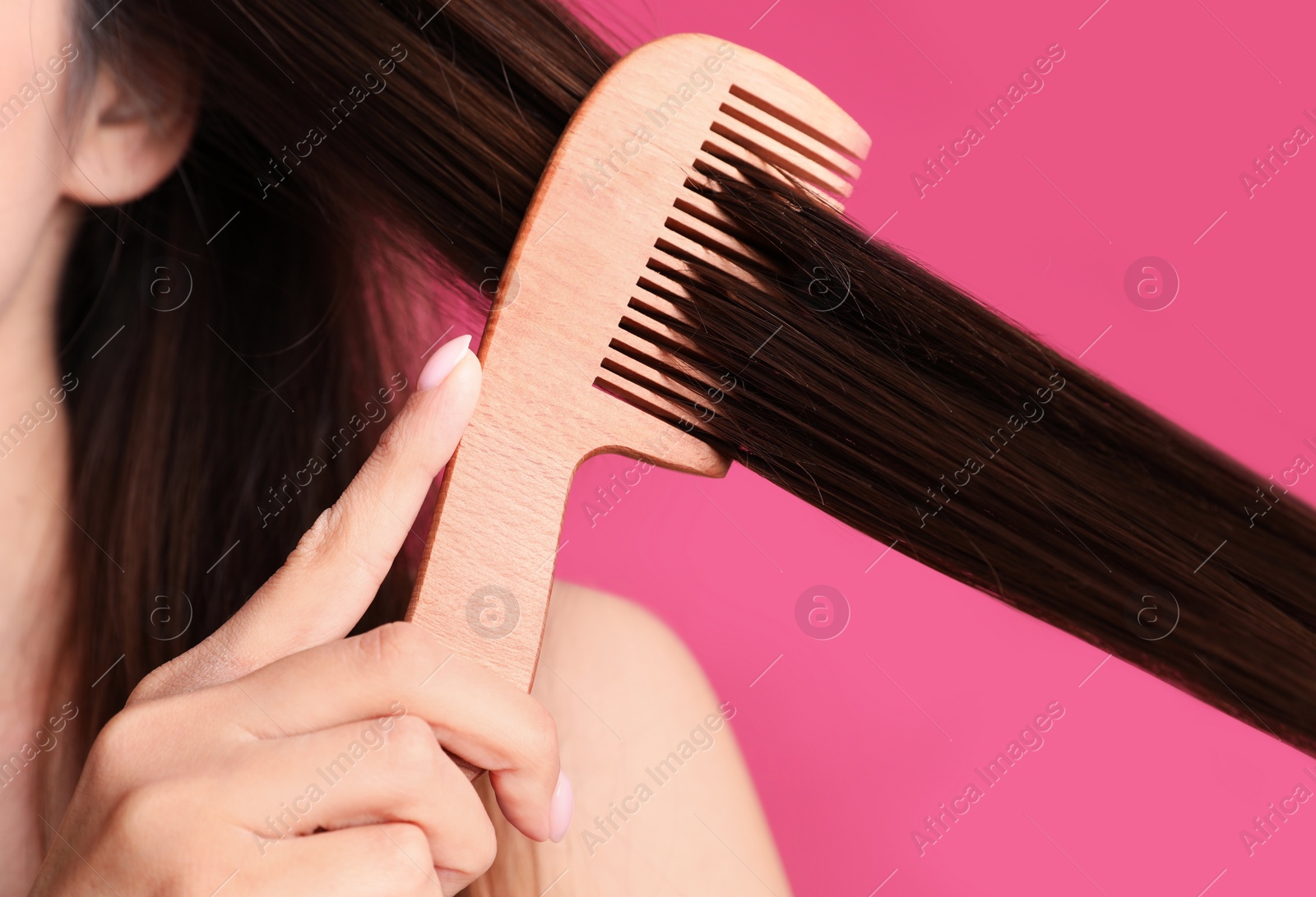 Photo of Young woman with wooden hair comb on color background, closeup