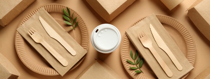 Image of Paper and wooden tableware with green twigs on beige background, flat lay. Banner design