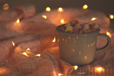 Cup of delicious hot cocoa with marshmallows and fairy lights on pink sweater, bokeh effect